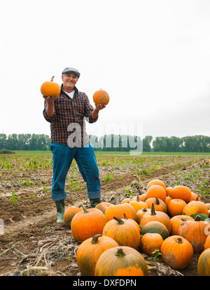 Bauer im Feld stehen, hält Kürbisse in Händen, neben Kürbis Ernte, Deutschland Stockfoto