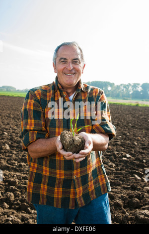 Porträt der Bauer im Feld stehen, halten Sämling Pflanze von Ernte, Deutschland Stockfoto