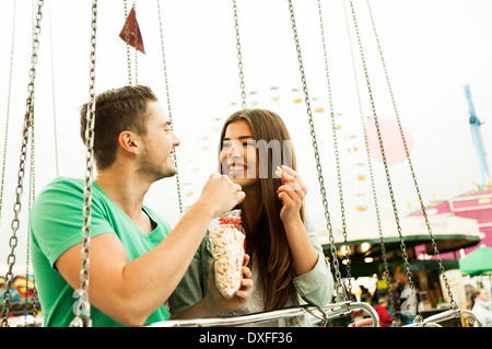 Junges Paar sitzt auf Vergnügungspark fahren Essen Popcorn, Deutschland Stockfoto