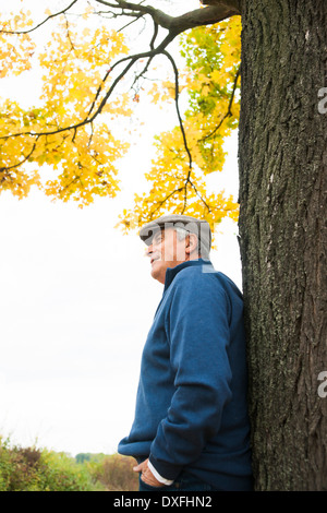 Senior-Mann lehnte sich gegen Baum im Herbst, Mannheim, Baden-Württemberg, Deutschland Stockfoto