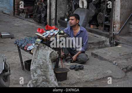 ein Mann verkauft Autohupen in Old Delhi kniet hinter seinem stall Stockfoto