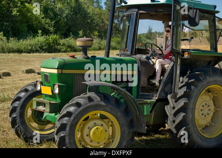 Teengirl fährt einen Traktor ziehen eines Anhängers durch eine Heu-Feld Stockfoto