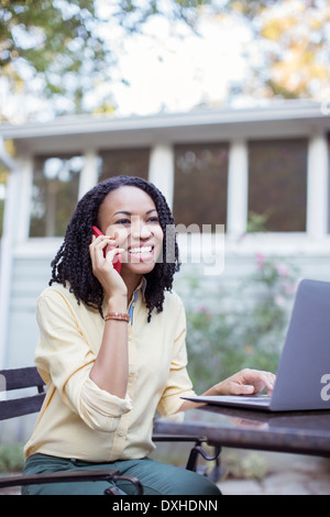 Glückliche Frau am Handy am Laptop auf Terrasse Stockfoto