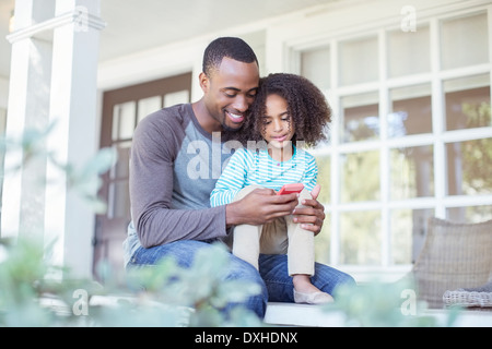 Vater und Tochter mit Handy auf Veranda Stockfoto