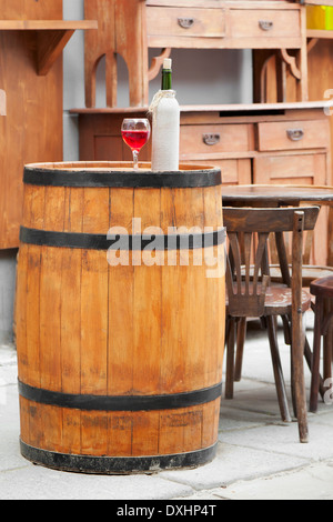 Holzfass mit Flaschen Wein und Glas, Stuhl und Tisch im Café im freien Stockfoto