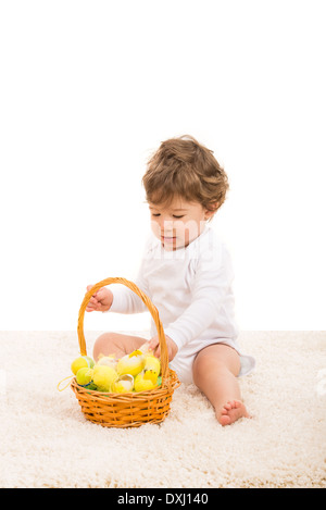 Kleinkind Jungen arrangieren Ostereier in einen Korb und sitzen auf Fell Teppich Stockfoto