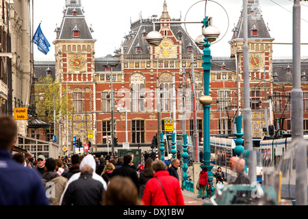 Fußgänger zu Fuß entlang Damrak in Amsterdam. Der Bahnhof Centraal ist im Hintergrund. Stockfoto