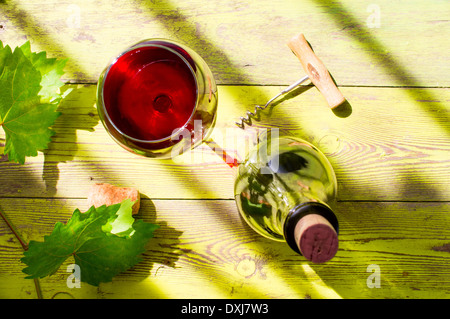 Glas Rotwein auf einem Holztisch mit Blättern von Trauben, Korkenzieher und Weinkorken und Flasche Wein. Stockfoto