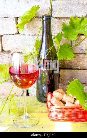 Eine Flasche Rotwein und einem Glas Wein neben einen Korb mit Weinkorken. Stockfoto