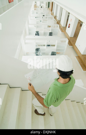 Mann mit harten Hut stehen im neuen Amt hält Pläne Stockfoto