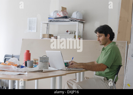 Mann mit Laptop auf behelfsmäßigen Schreibtisch im Baubüro Architekt Stockfoto