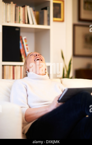 Porträt der schöne alte Frau mit tablet-pc und lächelnd, sitzt zu Hause auf Sofa Stockfoto