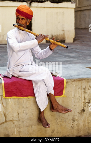 Indischer Musiker sitzt auf einer Mauer Flötenspiel in Mehrangarh Fort in Jodhpur, Indien Stockfoto