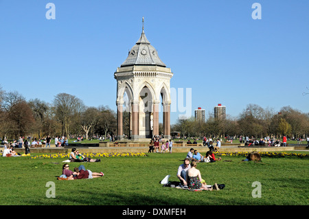 Menschen sitzen auf dem Rasen im Victoria Park mit dem Burdett-Coutts Memorial Trinkbrunnen Tower Hamlets London England UK Stockfoto