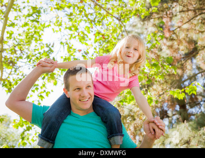 Süße junge Mädchen reitet Huckepack auf Papas Schultern draußen im Park. Stockfoto