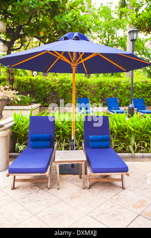 Zwei Stühle mit Sonnenschirmen in der Nähe von Schwimmbad im Luxushotel Stockfoto