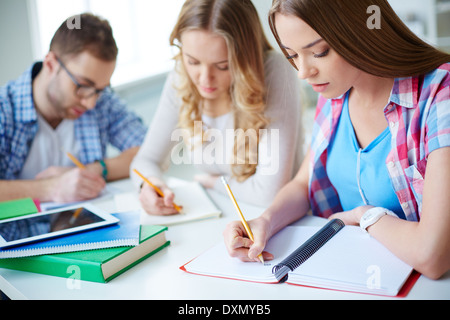 Kluges Mädchen und ihre Kollegen auf Hintergrund Durchführung schriftliche Aufgabe zur Lektion Stockfoto