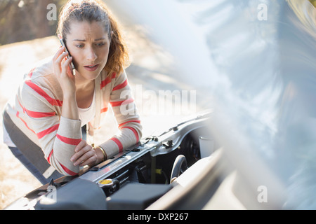 Frustrierte Frau reden über Handy und mit Blick auf Auto-Motor am Straßenrand Stockfoto