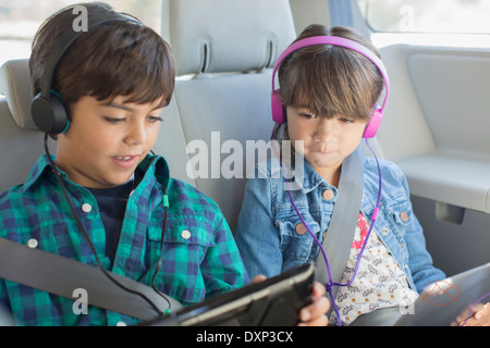 Bruder und Schwester mit Kopfhörern mit digitalen Tabletten im Rücksitz des Wagens Stockfoto