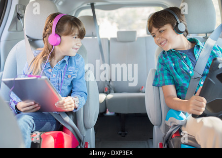 Glücklich Bruder und Schwester mit Kopfhörern mit digitalen Tabletten im Rücksitz des Wagens Stockfoto