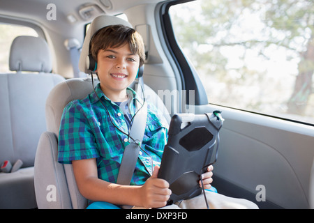 Porträt von fröhlicher Junge mit Kopfhörern mit digital-Tablette im Rücksitz des Wagens Stockfoto