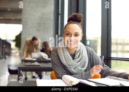 Glückliche junge Frau sitzt in der Bibliothek mit Büchern. Fröhliche junge Studentin Abschlussprüfungen vorbereiten. Stockfoto