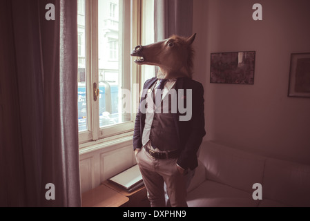 Pferd-Maskenmann vor Fenster zu Hause Stockfoto