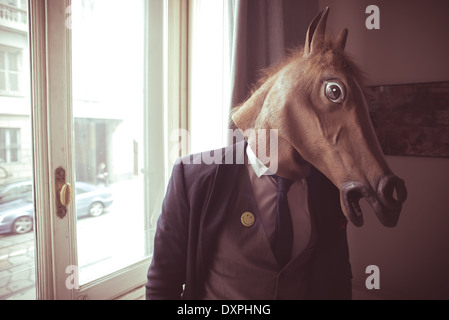 Pferd-Maskenmann vor Fenster zu Hause Stockfoto