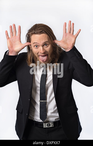 Ein bärtiger Langhaar-Mann in Anzug mit lustigen Ausdruck, seine Zunge heraus, Hände hoch. Ein humorvolles Porträt-Konzept Stockfoto