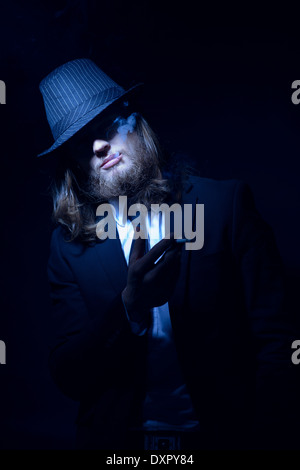 Ein bärtiger lange Haare Mann einen Fedora Hut und Anzug Rauchen Stockfoto