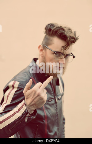 Ein bärtiger Mann in Vintage Pompadour Frisur und Vintage Brillen spiegeln seinen Mittelfinger, eine trendige Vintage Porträt-Konzept Stockfoto