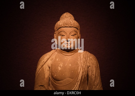 Foto einer alten Buddha-Skulptur von einem Scheinwerfer vor einem dunklen lila Hintergrund beleuchtet. Stockfoto