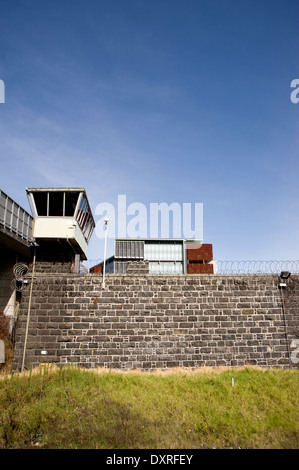 Gefängnismauern und Wachturm gegen blauen Himmel. Alte Steinmauern Kontrast gegen den neuen Baustein im Hintergrund. Stockfoto