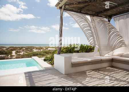 Vorhänge wehen im Wind auf Luxus-Pool-Terrasse mit Blick auf Meer Stockfoto