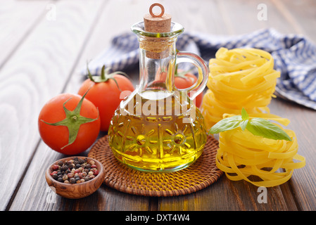 Olivenöl in Glasflasche mit Nudeln, Tomaten und Basilikum auf hölzernen Hintergrund Stockfoto