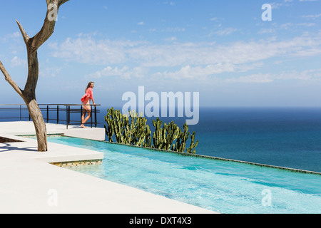 Frau stehend auf Pool-Balkon mit Blick auf Meer Stockfoto