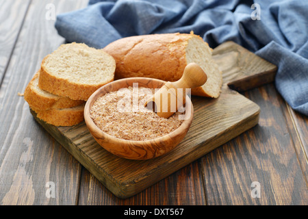 Weizenkleie in Schüssel mit geschnittenem Brot auf hölzernen Hintergrund Stockfoto
