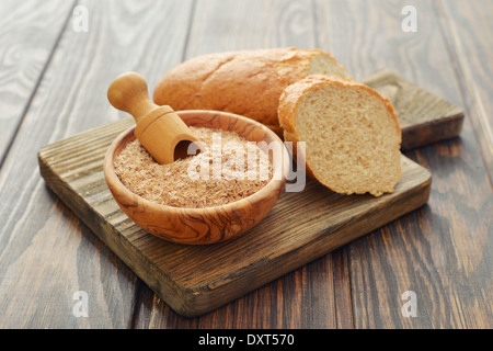 Weizenkleie in Schüssel mit geschnittenem Brot auf hölzernen Hintergrund Stockfoto