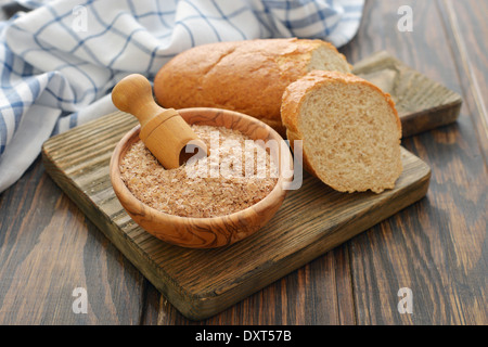 Weizenkleie in Schüssel mit geschnittenem Brot auf hölzernen Hintergrund Stockfoto