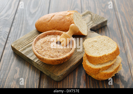 Weizenkleie in Schüssel mit geschnittenem Brot auf hölzernen Hintergrund Stockfoto