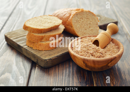 Weizenkleie in Schüssel mit geschnittenem Brot auf hölzernen Hintergrund Stockfoto