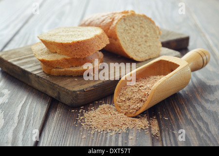 Weizenkleie in Schaufel mit geschnittenem Brot auf hölzernen Hintergrund Stockfoto
