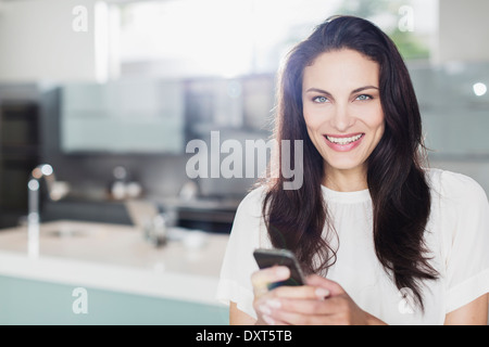 Porträt von lächelnden Frau SMS mit Handy in Küche Stockfoto