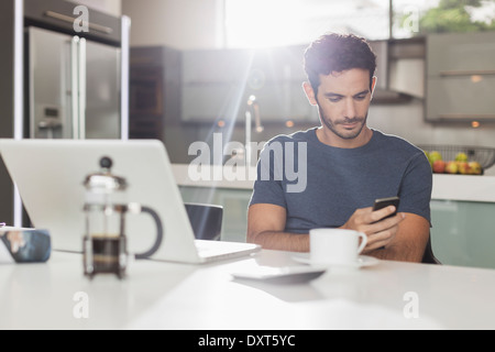 Mann SMS mit Handy am Küchentisch Stockfoto