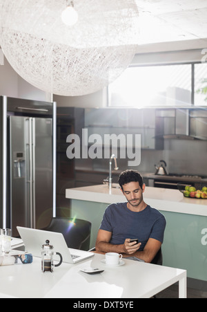 Mann SMS mit Handy am Küchentisch Stockfoto