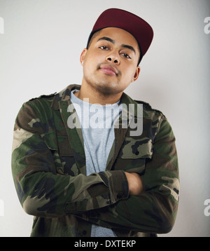 Lässige junger Mann tragen Camouflage Jacke und Mütze mit seinen Armen gekreuzt, Blick in die Kamera mit Haltung. Junge männliche Model. Stockfoto