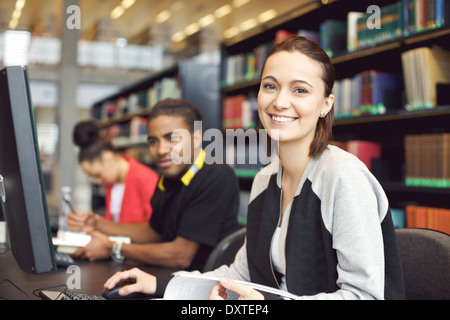 Schönen jungen kaukasischen Studenten sitzen am Tisch mit Blick auf die Kamera zu Lächeln-Computer. Junge Studenten. Stockfoto