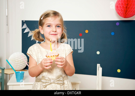 Mädchen auf der Geburtstagsparty halten Cupcake Wit brennende Kerze, München, Bayern, Deutschland Stockfoto