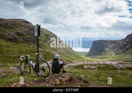 Ein Radfahrer liegt teilweise bis Großbritanniens längsten Straße klettern in Lochcarron Schottland. Rückblickend auf die Leistung Stockfoto