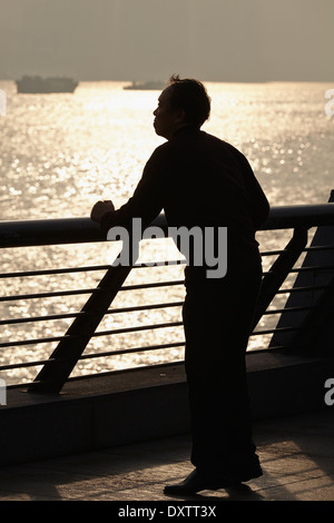 Ein Mann machte gegen die aufgehende Sonne Silhouetten und machte am frühen Morgen Übungen auf dem Flussufer Bund in Shanghai, China. Stockfoto